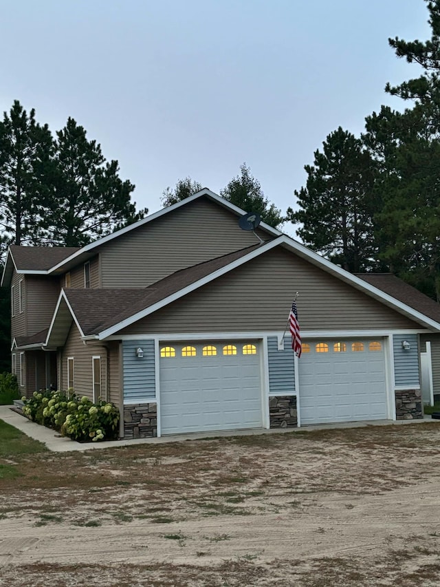 multi unit property featuring a garage, stone siding, and dirt driveway