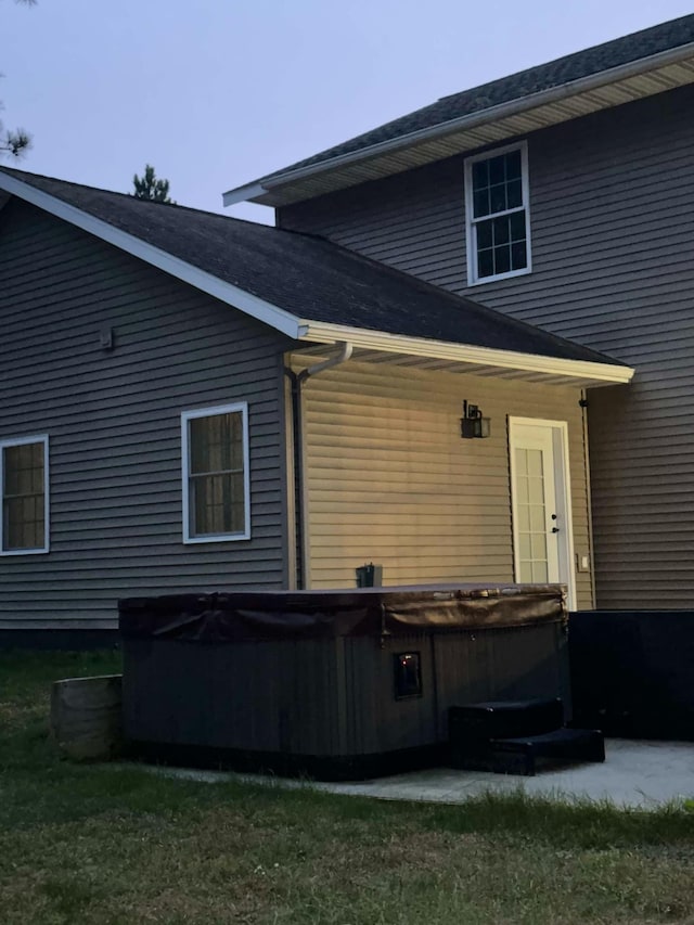 back of property featuring a yard and a hot tub