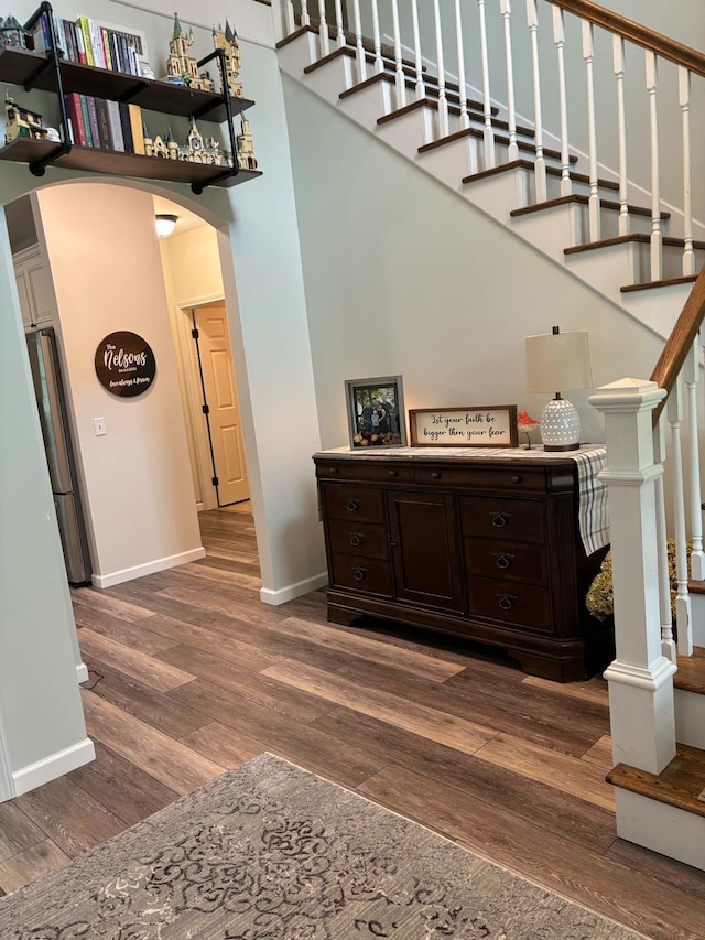 staircase featuring wood finished floors, baseboards, and arched walkways