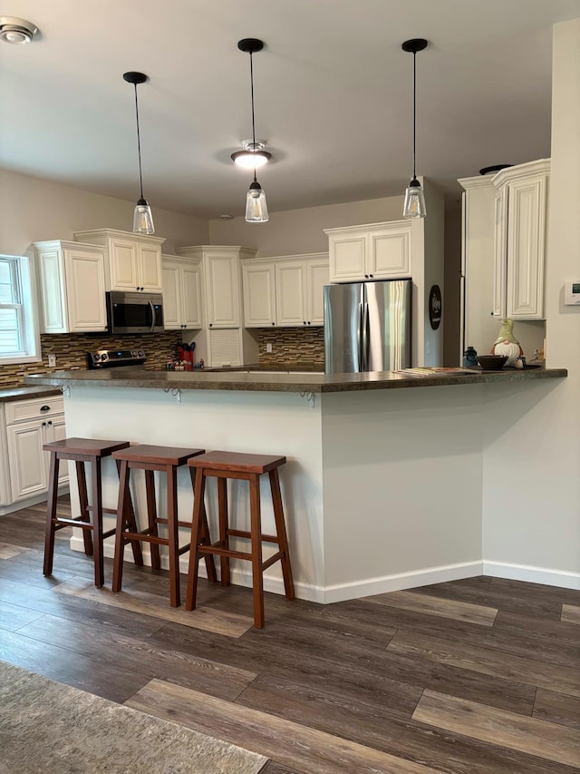 kitchen featuring dark wood-type flooring, a breakfast bar area, decorative backsplash, appliances with stainless steel finishes, and hanging light fixtures