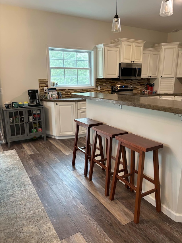 kitchen with a kitchen breakfast bar, dark countertops, stainless steel appliances, decorative backsplash, and dark wood-style flooring