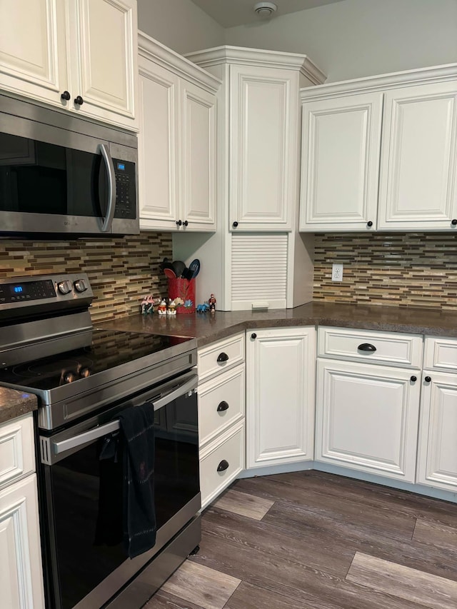 kitchen featuring dark wood finished floors, appliances with stainless steel finishes, white cabinetry, dark countertops, and backsplash