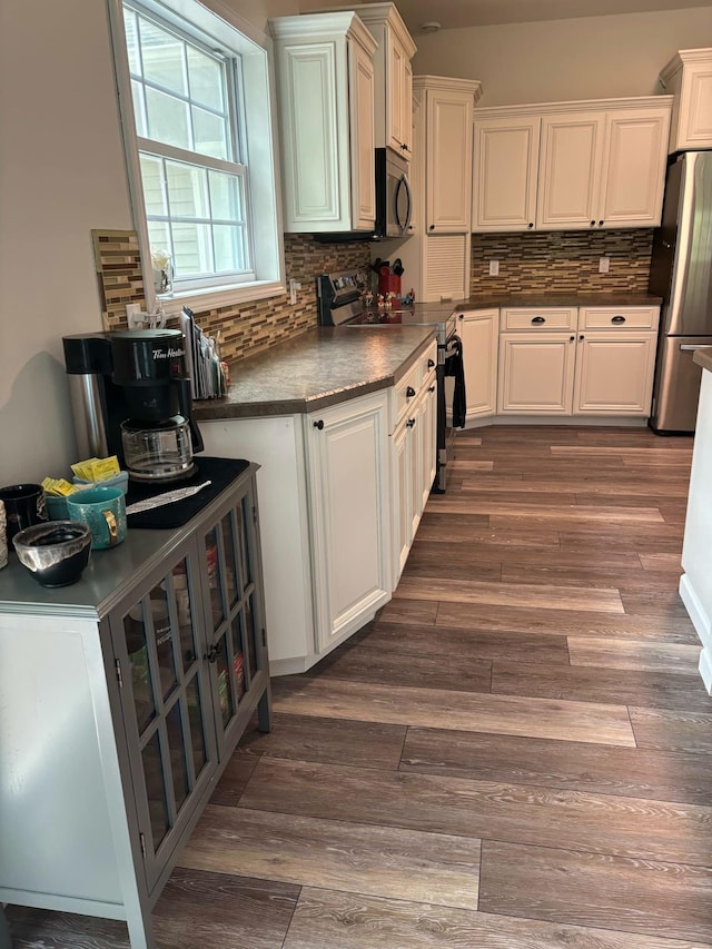 kitchen with dark countertops, dark wood finished floors, decorative backsplash, appliances with stainless steel finishes, and white cabinets