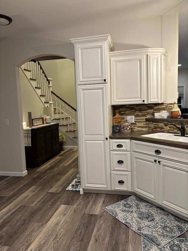 bar with a sink, tasteful backsplash, dark wood finished floors, arched walkways, and stairs