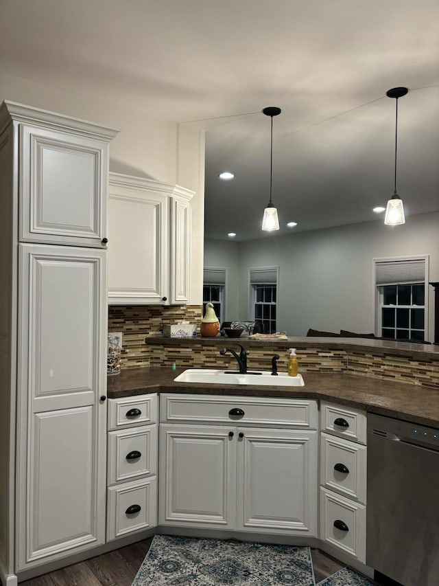 kitchen with a sink, white cabinets, stainless steel dishwasher, dark countertops, and backsplash