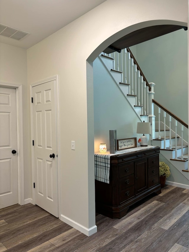 staircase featuring arched walkways, visible vents, baseboards, and wood finished floors