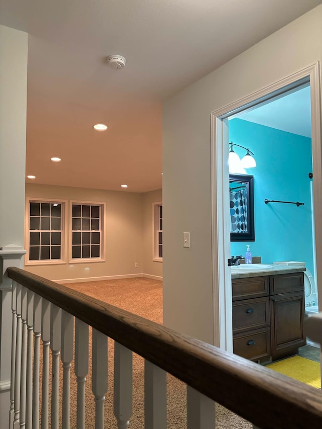 hallway featuring recessed lighting, light carpet, and a sink