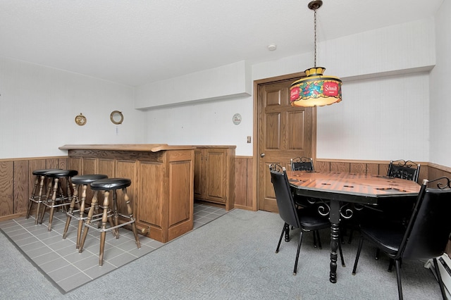 dining room with light carpet, a wainscoted wall, wood walls, and a bar