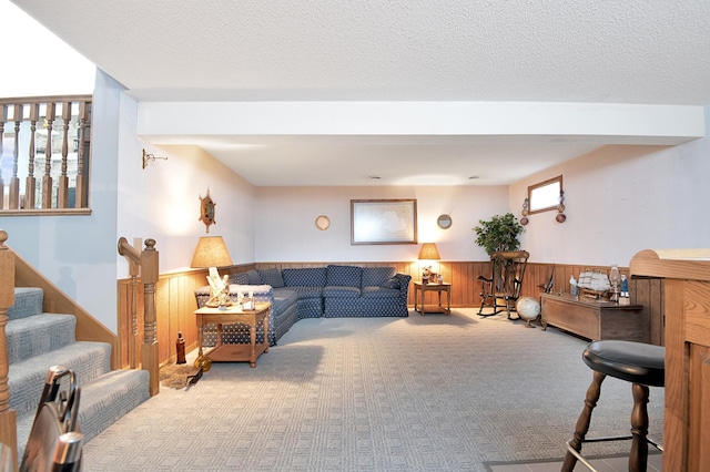 living area featuring carpet, stairway, wood walls, wainscoting, and a textured ceiling