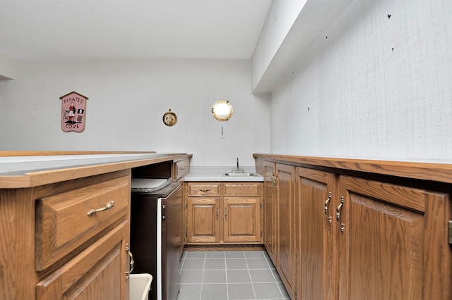 kitchen with light tile patterned floors, brown cabinetry, light countertops, and a sink