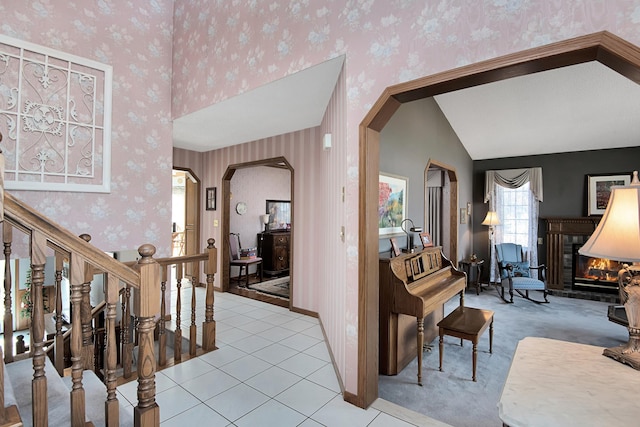 entryway featuring a glass covered fireplace, arched walkways, wallpapered walls, light tile patterned floors, and lofted ceiling