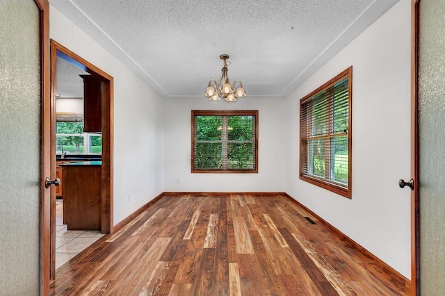 spare room with a textured ceiling, an inviting chandelier, wood finished floors, and a healthy amount of sunlight