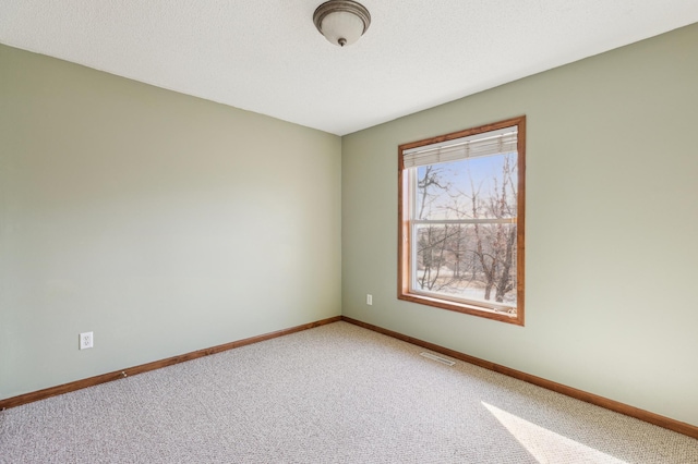 carpeted spare room featuring visible vents, baseboards, and a textured ceiling