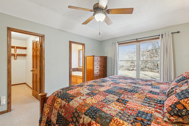 bedroom featuring light colored carpet, a textured ceiling, a walk in closet, and baseboards