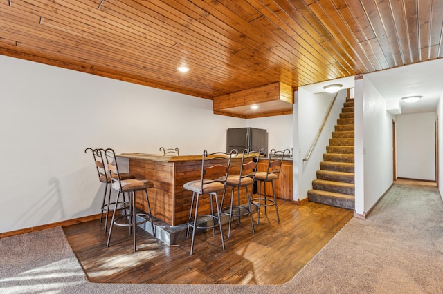 bar featuring stairway, wood finished floors, refrigerator, wood ceiling, and indoor bar