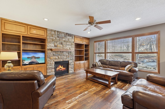 living room featuring recessed lighting, ceiling fan, a stone fireplace, dark wood-type flooring, and a textured ceiling