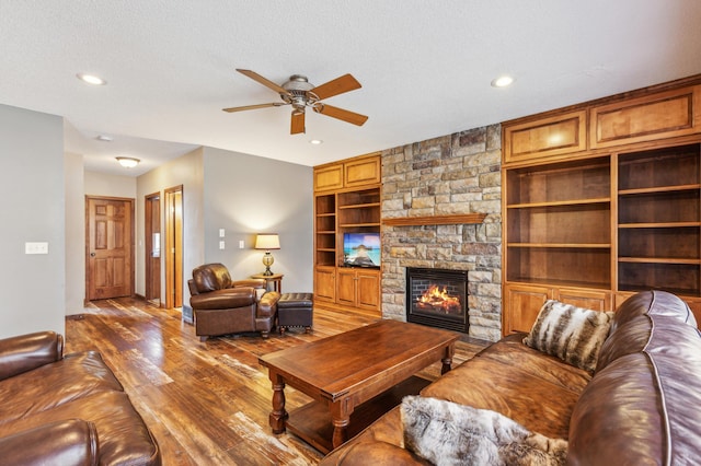 living room with a stone fireplace, recessed lighting, wood finished floors, a textured ceiling, and a ceiling fan