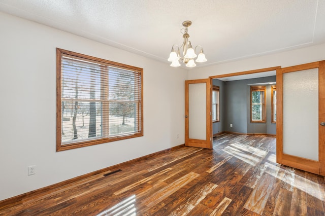 spare room featuring a chandelier, visible vents, a healthy amount of sunlight, and dark wood-type flooring