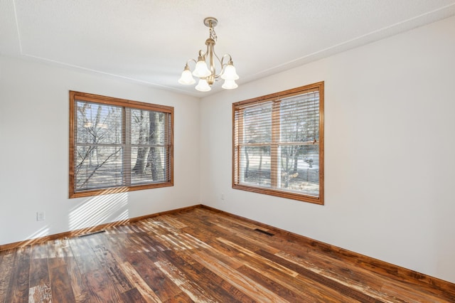 unfurnished room featuring a wealth of natural light, a chandelier, baseboards, and dark wood finished floors