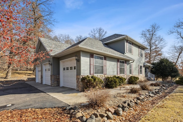 view of property exterior featuring stone siding, driveway, an attached garage, and a shingled roof