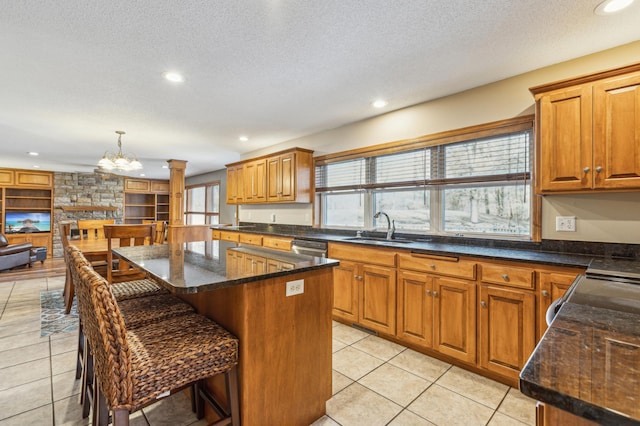 kitchen with a kitchen island, light tile patterned floors, a textured ceiling, ornate columns, and a sink