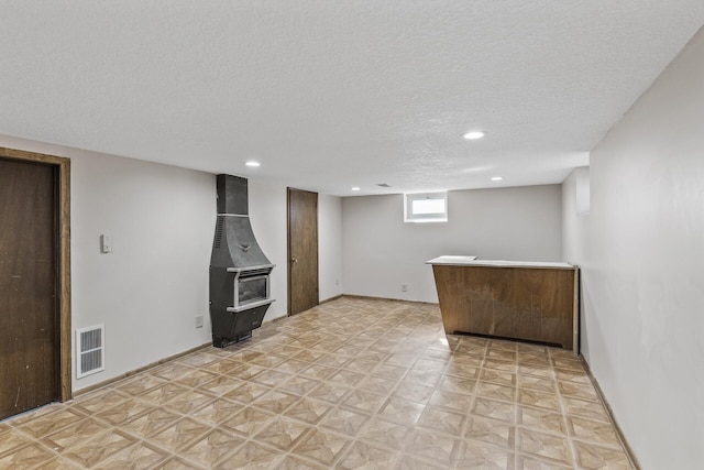 below grade area featuring visible vents, a textured ceiling, recessed lighting, baseboards, and a wood stove