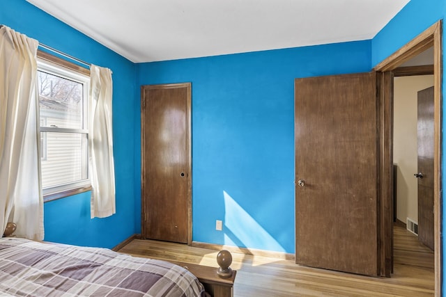 unfurnished bedroom with a closet, visible vents, baseboards, and wood finished floors