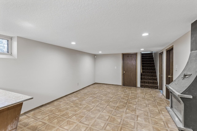 basement with light floors, baseboards, recessed lighting, stairs, and a textured ceiling