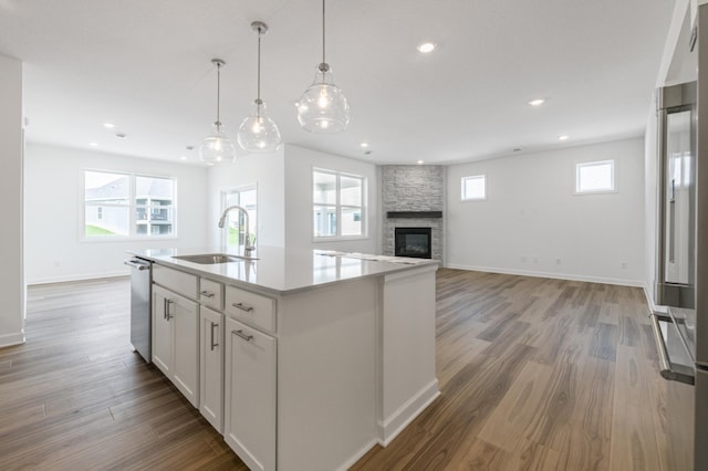 kitchen featuring a stone fireplace, white cabinetry, wood finished floors, and a sink