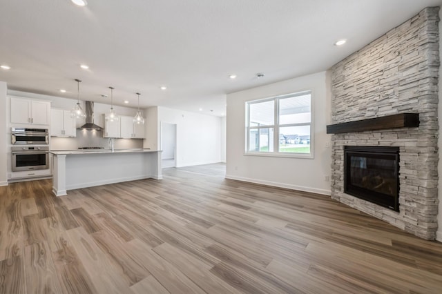 unfurnished living room featuring baseboards, recessed lighting, a fireplace, a sink, and light wood-style floors