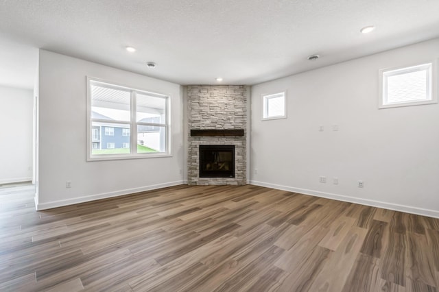 unfurnished living room featuring a textured ceiling, wood finished floors, recessed lighting, a fireplace, and baseboards