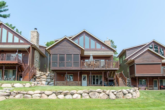 rear view of property featuring faux log siding, a wooden deck, stairs, a lawn, and a chimney