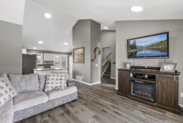 living room featuring visible vents, baseboards, stairway, lofted ceiling, and wood finished floors