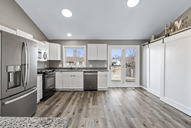 kitchen featuring a sink, vaulted ceiling, appliances with stainless steel finishes, white cabinetry, and a barn door