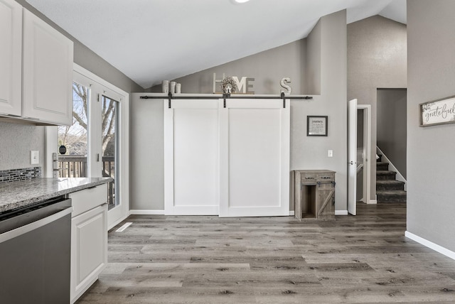 kitchen with light wood-type flooring, a barn door, stainless steel dishwasher, and white cabinets