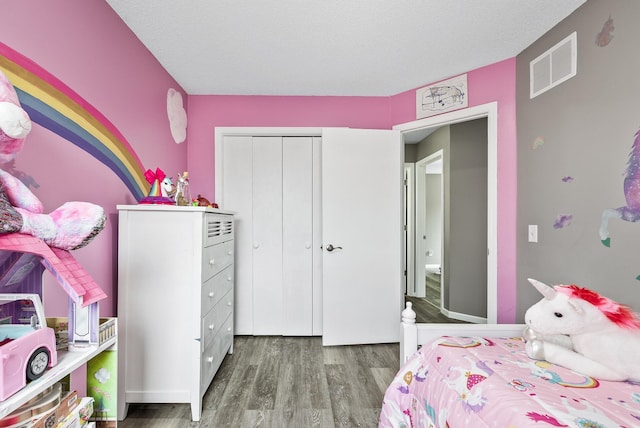 bedroom featuring a closet, visible vents, a textured ceiling, and wood finished floors