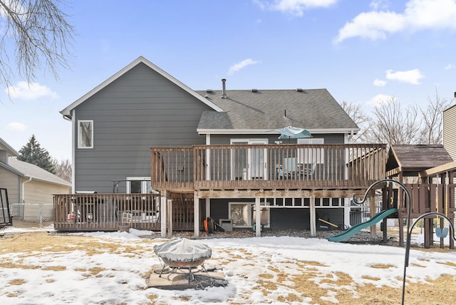 snow covered property featuring a wooden deck, a shingled roof, and a playground