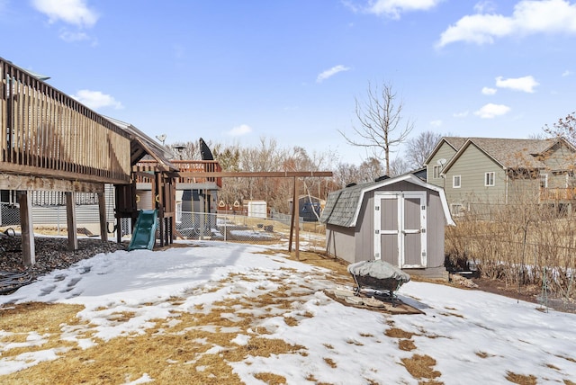 snowy yard featuring a storage unit, a playground, an outbuilding, and fence