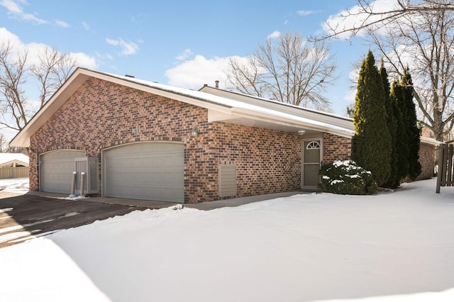 view of snow covered exterior with brick siding and an attached garage