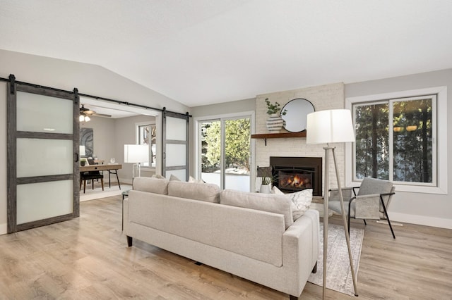 living room featuring light wood-style flooring, a barn door, baseboards, a brick fireplace, and vaulted ceiling