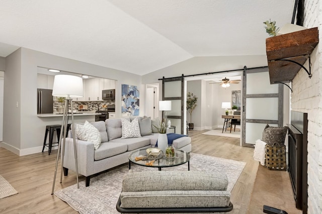 living area featuring baseboards, lofted ceiling, a barn door, a fireplace, and light wood-style floors