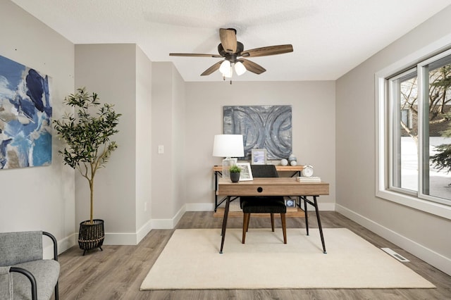 office space featuring visible vents, baseboards, light wood-style floors, and ceiling fan
