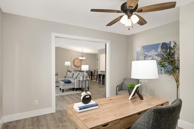 home office featuring baseboards, a textured ceiling, ceiling fan with notable chandelier, and light wood finished floors