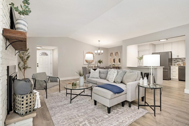 living room with vaulted ceiling, a fireplace, light wood finished floors, and a chandelier