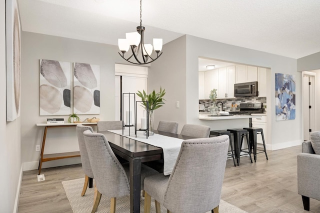 dining space with a chandelier, baseboards, a textured ceiling, and light wood-style flooring