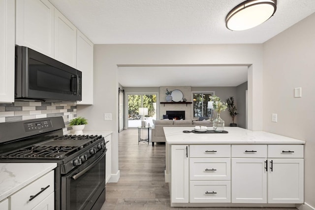 kitchen with a large fireplace, backsplash, black range with gas cooktop, and white cabinetry