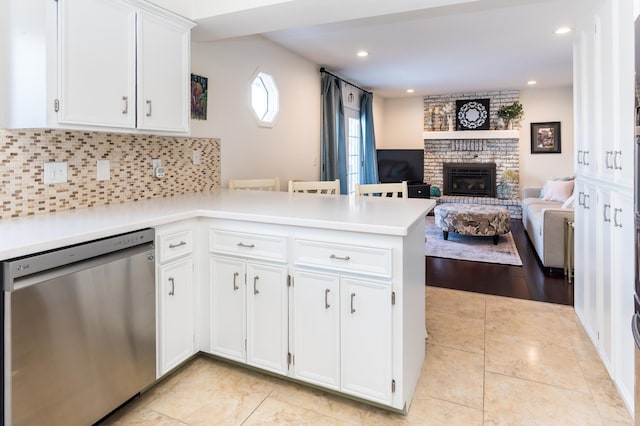 kitchen featuring a peninsula, light countertops, white cabinets, dishwasher, and a brick fireplace