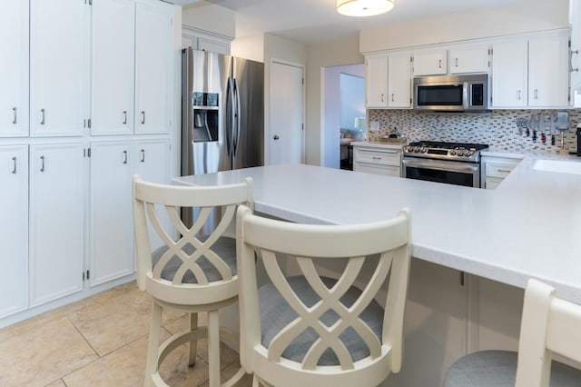 kitchen featuring backsplash, stainless steel appliances, white cabinets, light countertops, and light tile patterned floors