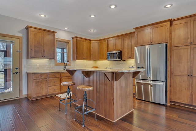 kitchen featuring brown cabinetry, appliances with stainless steel finishes, a breakfast bar area, and dark wood finished floors