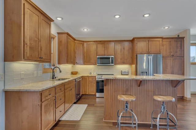 kitchen with a center island, a breakfast bar, appliances with stainless steel finishes, dark wood-style floors, and a sink